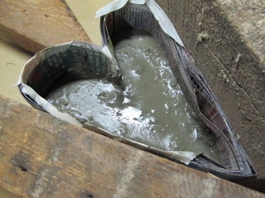 Portland cement mixed thick, being poured and scooped into the mold. Beginning to settle.