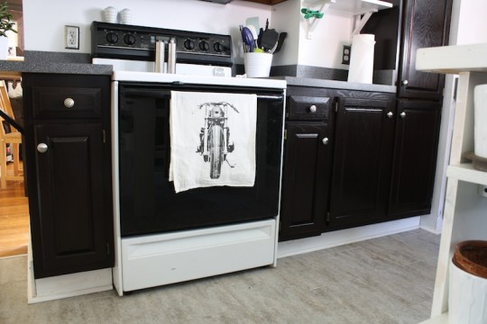 Kitchen cabinets, refinished with dark brown stain and adorned with a new tea towel.